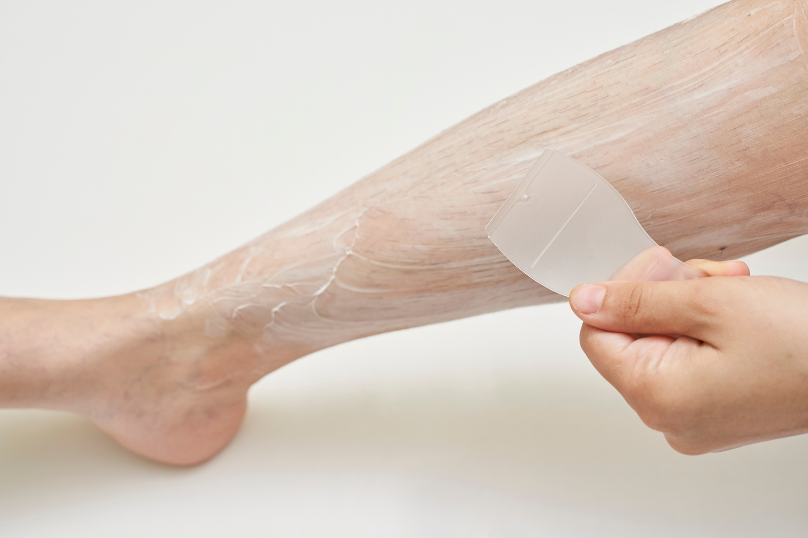 A woman applying a layer of depilatory cream over the leg hairs