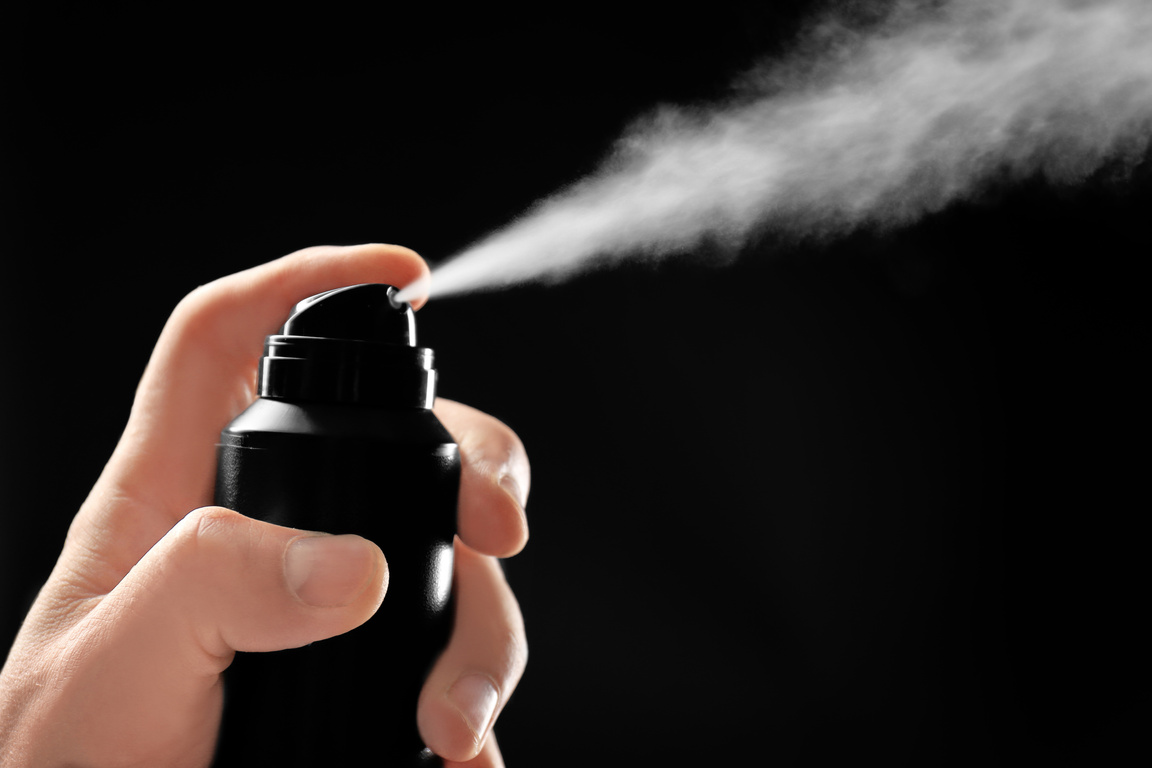 Man Spraying Deodorant on Dark Background